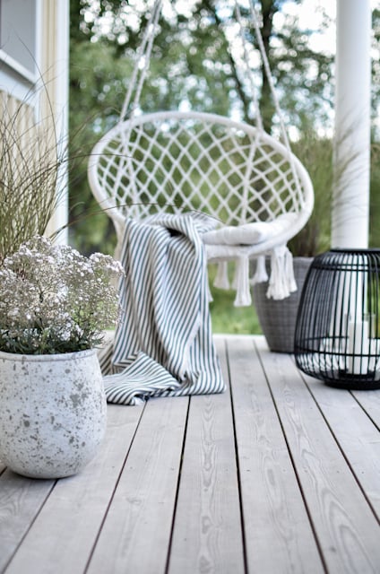 Hängstol med en randig filt på en träveranda med krukväxter och en svart dekorationslampa.