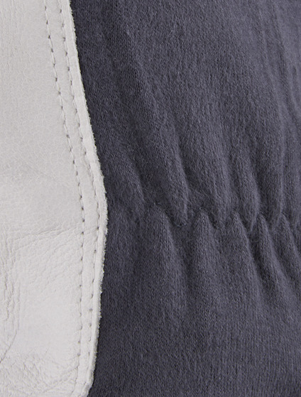 Närbild av en grå textil med resårdetalj och vit läderkant.