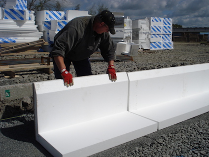 Person hanterar vita skivor av expanderad polystyren på en grusplan. Fler skivor staplade i bakgrunden.