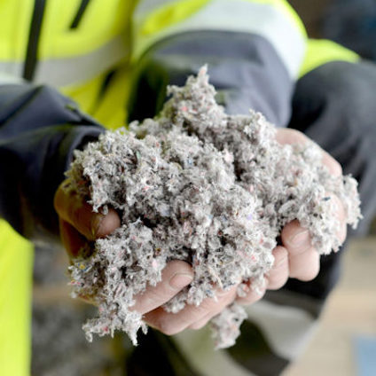 Person i reflexjacka håller i en hög med grått, fibrigt material i händerna.