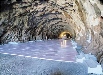 En tunnel med ett nylagt golv täckt av rosa isoleringsplattor och stenigt tak och väggar.