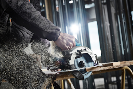Person använder en cirkelsåg för att såga trä, gnistor och sågspån sprutar ut i en byggmiljö.