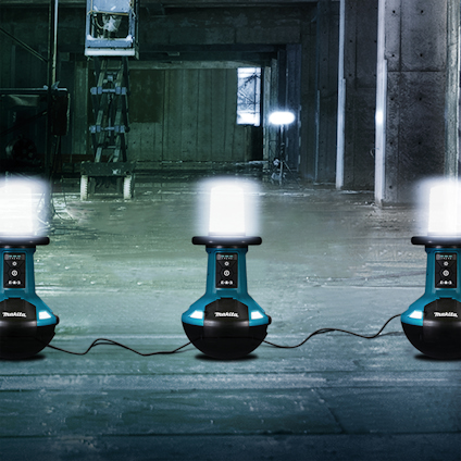 Tre Makita-lampor placerade i rad på ett golv i en mörk industriell miljö.