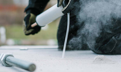 En person använder en luftpump för att blåsa rent ett borrhål i betong. Damm stiger upp.