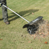 Person using a Makita tool on a lawn, with grass clippings and leaves being displaced.
