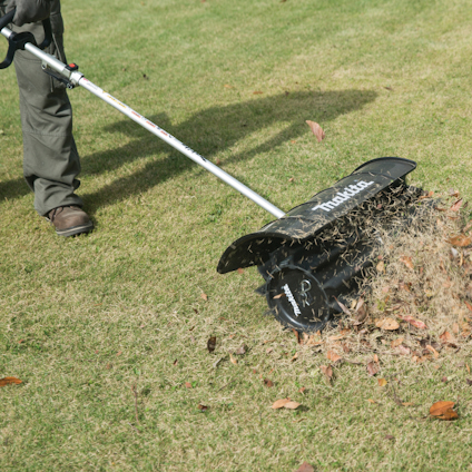 Person using a Makita tool on a lawn, with grass clippings and leaves being displaced.