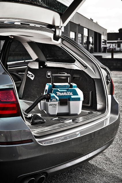 Öppen bagagelucka på en bil med en blå Makita dammsugare inuti.