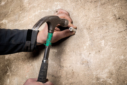 Händer använder en hammare för att slå in en lättbetongplugg i en betongvägg.