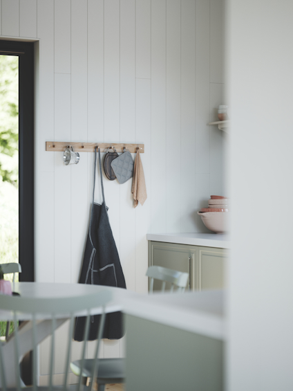 Kök med träpanel, kroklist med förkläde och grytlappar, grön skåp och skålar.