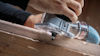 Hand som använder en handöverfräs på en träbit med ett blått dammutsug anslutet.