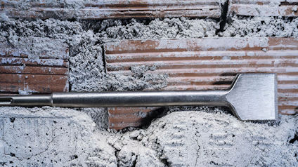 Metallmejsel ovanpå en delvis nedriven tegelvägg med murbruk och damm.