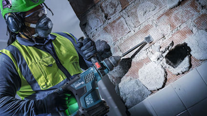 Person i skyddsutrustning bryter kaklat tegel med en kraftig borrmaskin.