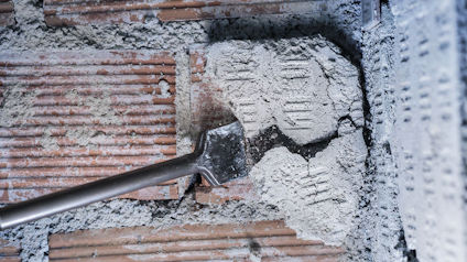 Hammare krossar tegelvägg, exponerar sprickor och damm.